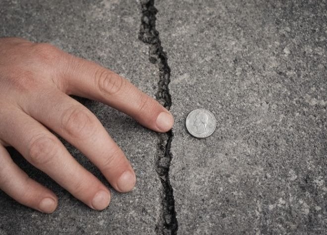Hand testing a sidewalk crack for height difference with a coin for scale