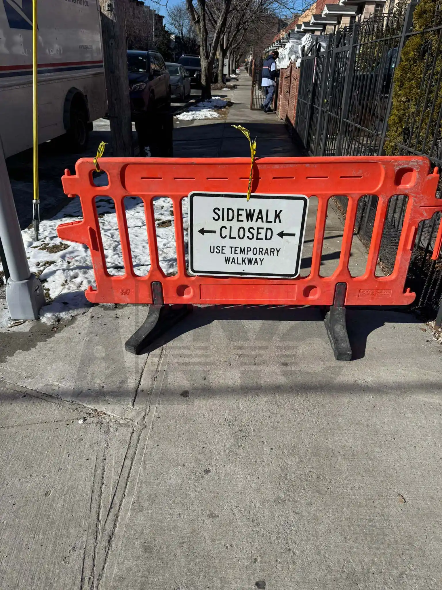 A cracked sidewalk with uneven concrete slabs is next to a grassy area in a residential neighborhood.